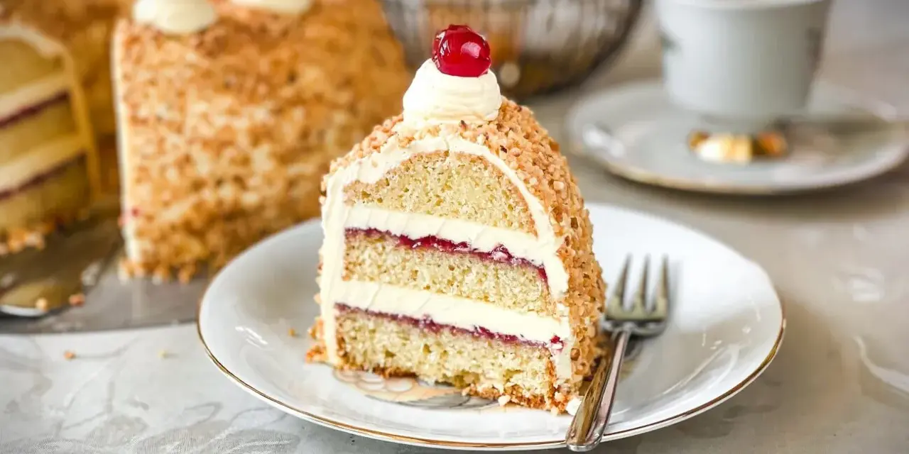 Ein Stück Frankfurter Kranz, das Rezept eines Konditors, mit Buttercreme und Kirschen verziert, umgeben von gehackten Nüssen.