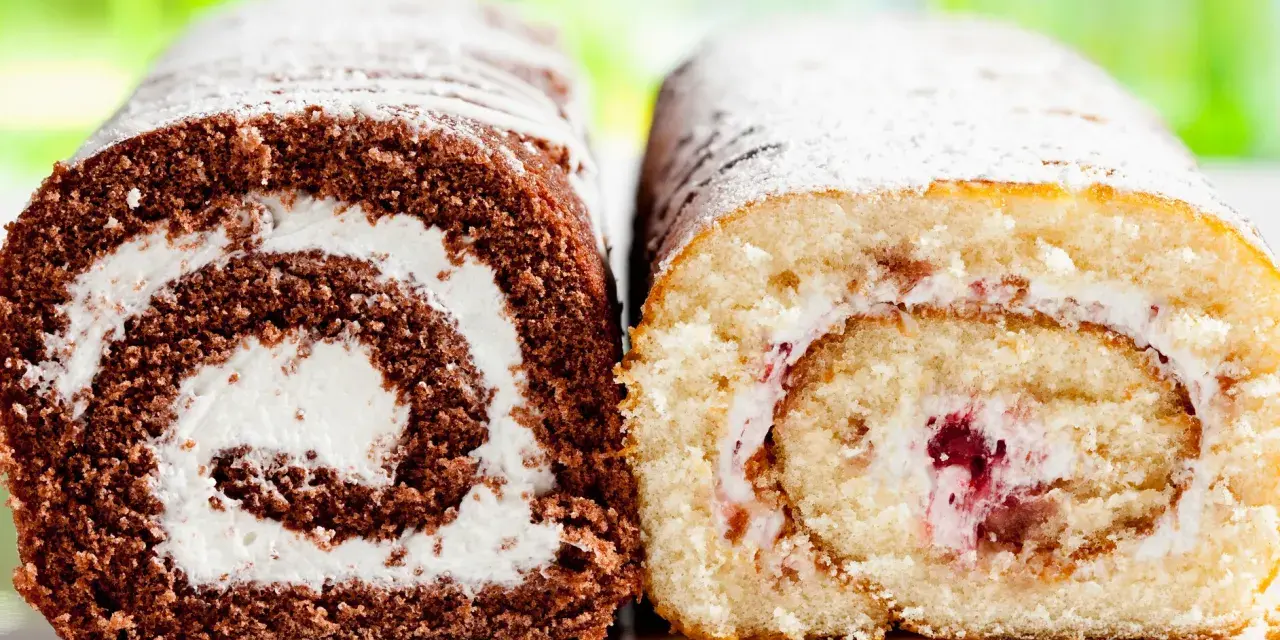 Zwei Biskuitrollen, eine schokoladig, die andere hell, mit Sahne und Fruchtfüllung, bestäubt mit Puderzucker. Wie von Landfrauen gebacken.