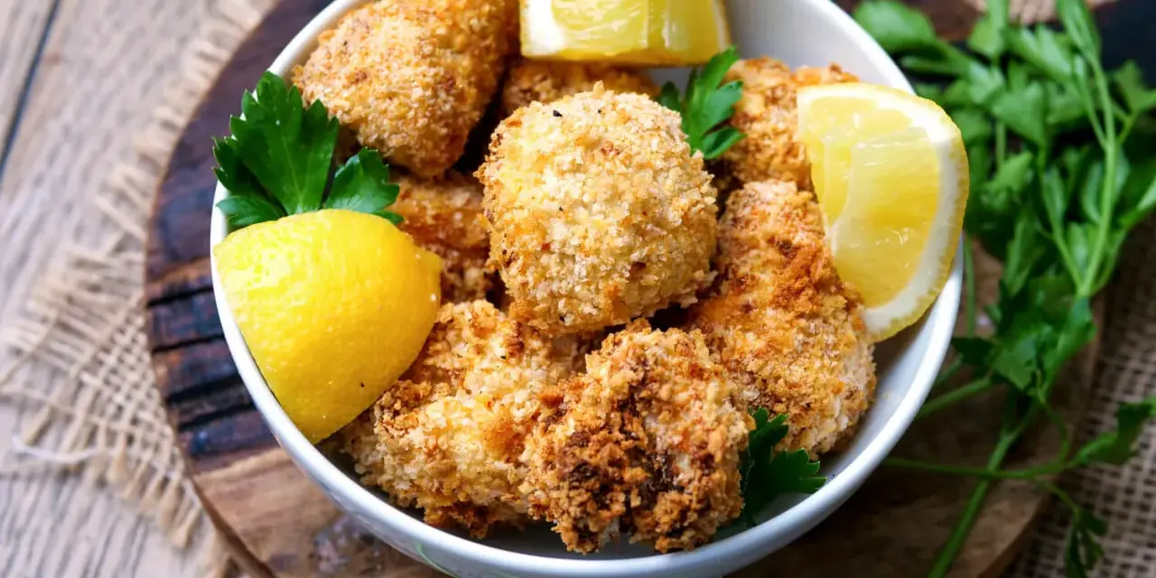 Knuspriger blumenkohl im airfryer, goldbraun paniert, serviert mit frischen Zitronenspalten und Petersilie.
