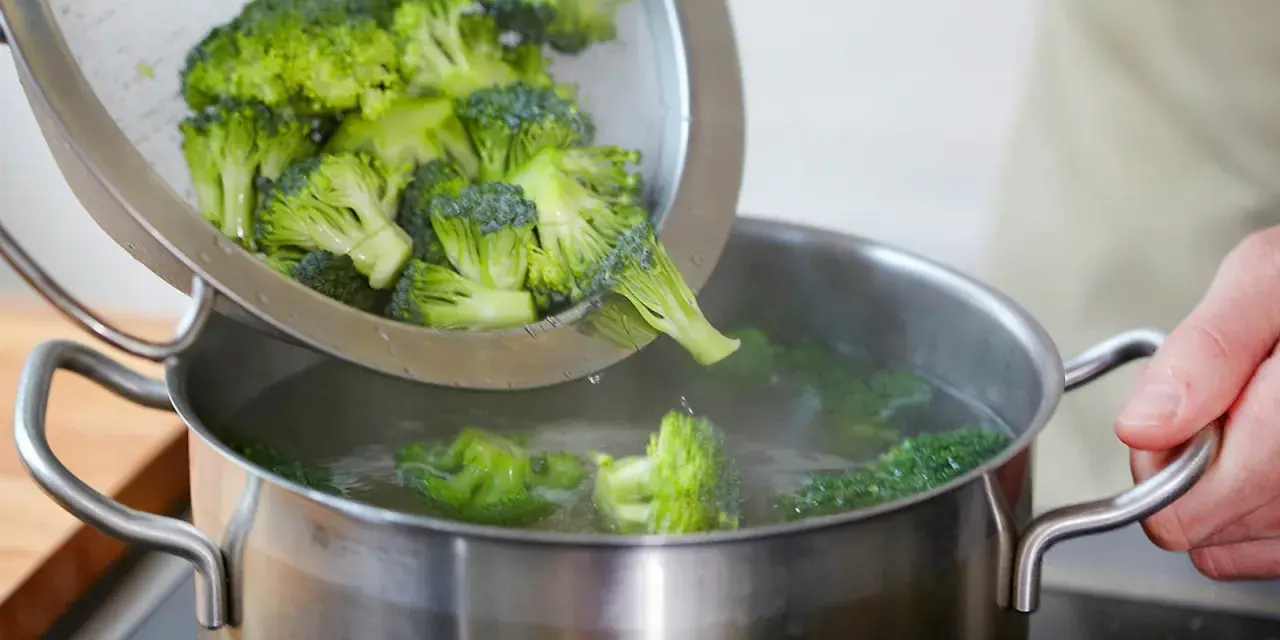 Frischer Brokkoli wird aus einem Sieb in einen Topf mit kochendem Wasser gegeben. Perfekt für eine gesunde Brokkoli-Pfanne.