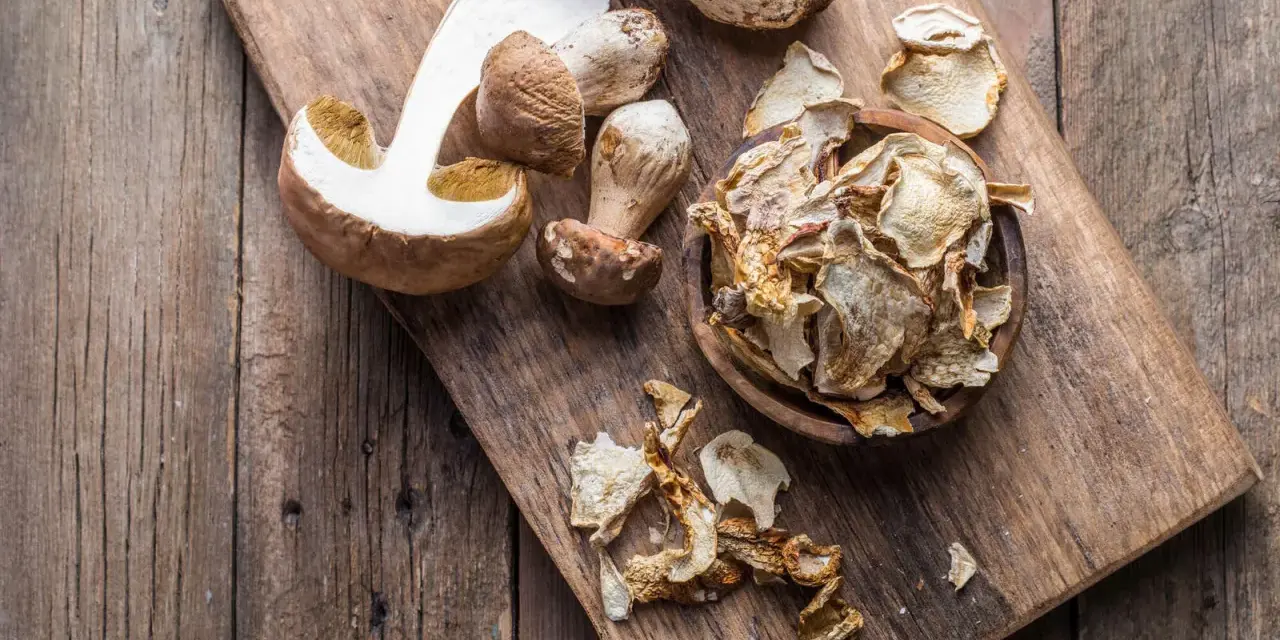 Frische und getrocknete Steinpilze liegen auf einem Holzbrett. Die getrockneten Pilze sind in einer Schale und daneben verteilt, bereit zum Kochen.