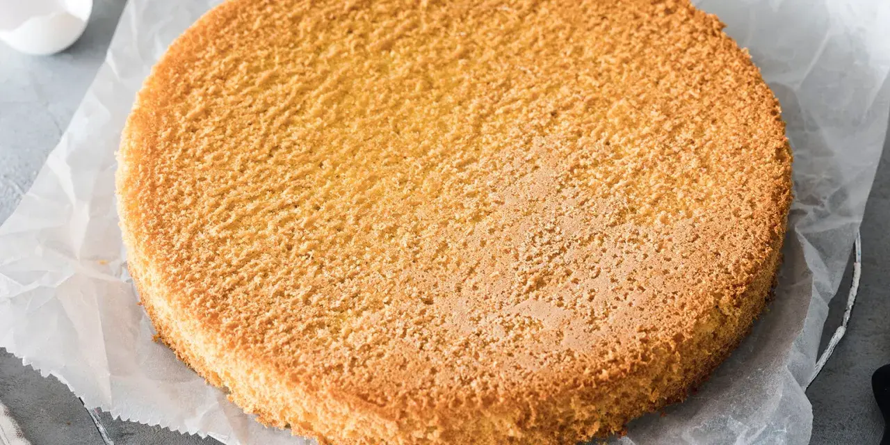 Ein goldbrauner, luftiger Biskuitboden auf Backpapier, bereit für ein köstliches Biskuitboden Rezept.