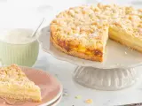 Ein saftiger Streuselkuchen mit Puddingfüllung, bestäubt mit Puderzucker. Daneben eine Tasse Cappuccino.