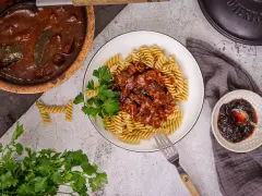 Herzhaftes Gulasch gemischt Rezept mit Fusilli, garniert mit Petersilie. Daneben ein kleiner Teller mit Preiselbeeren.