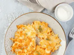 Knusprige Kartoffelpuffer, im Waffeleisen goldbraun gebacken, liegen auf einem Teller. Dazu ein Schälchen mit Sour Cream und ein Gabel.