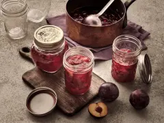 Frisch eingekochte Pflaumenmarmelade im Glas, bereit für das pflaumenmarmelade rezept. Frische Pflaumen liegen daneben.