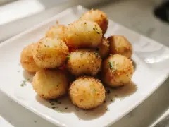 Goldbraune, knusprige kroketten aus kartoffelbrei, garniert mit Petersilie, auf einem weißen Teller.