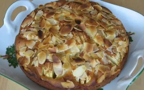 Ein köstlicher, kleiner Apfelkuchen mit gerösteten Mandelblättchen auf einer verzierten Servierplatte.