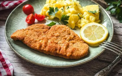 Perfekt gebratenes Putenschnitzel mit Kartoffelsalat, Tomaten und Zitrone auf einem Teller.