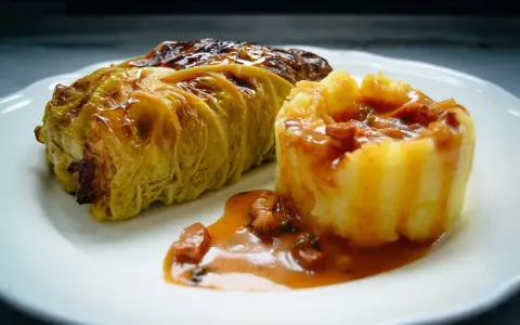Ein goldbraunes Kohlrouladen-Rezept auf einem Teller, serviert mit Kartoffelpüree und einer herzhaften Sauce.