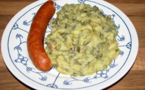 Omas Stielmus Rezept: deftiger Grünkohl mit Kartoffeln und einer herzhaften Bratwurst auf einem blau-weißen Teller.