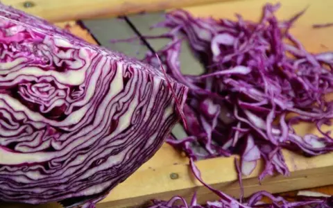Ein halber Rotkohl liegt auf einem Holzbrett, daneben fein geschnittener Rotkohl für einen Salat.