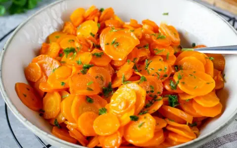 Schüssel mit glasierten Karottenscheiben, garniert mit Petersilie. Perfekt gekochte Karotten, die Lust auf mehr machen.