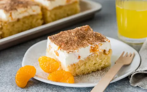 Ein saftiges Stück Fantakuchen-Rezept mit Mandarinen und Sahne, bestreut mit Zimt. Dazu ein Glas Fanta und frische Mandarinenstücke.