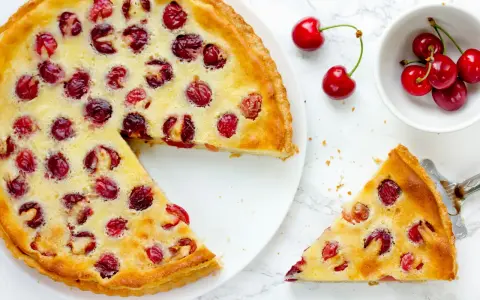Ein köstlicher Pudding Kirsch Kuchen, mit frischen Kirschen belegt und goldbraun gebacken. Ein Stück wird gerade serviert.