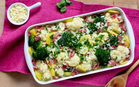 Ein herzhafter Blumenkohl-Brokkoli-Auflauf mit Kartoffeln und Schinken, bestreut mit frischer Petersilie und Käse.