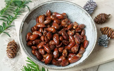 Schüssel mit glasierten, gebrannten Mandeln, zubereitet im Airfryer. Dekoriert mit Tannenzapfen und Tannenzweigen.
