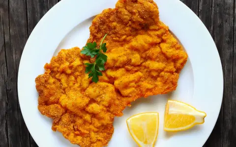 Ein knuspriges Schnitzel im Backofen, goldbraun paniert, mit Petersilie und Zitronenspalten auf einem weißen Teller serviert.