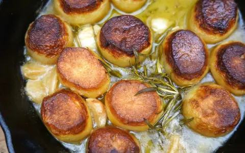 Saftige Fondant Kartoffeln mit Rosmarin und Knoblauch in einer Gusseisenpfanne, goldbraun gebraten.
