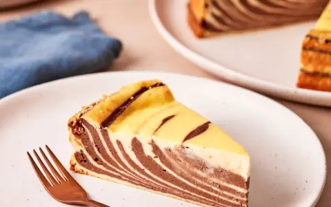 Ein Stück Zebrakuchen mit Quark, das auf einem Teller liegt, daneben eine Gabel.