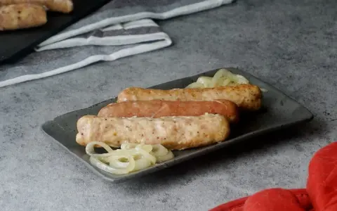 Drei Bratwürste mit Zwiebeln auf einem Teller, bereit zum Servieren. Sie sehen aus, als wären sie gerade aus dem Backofen gekommen.