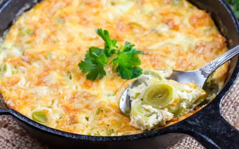 Ein goldbraunes Kartoffel-Lauch-Gratin in einer Gusseisenpfanne, mit einem Löffel herausgenommen, garniert mit Petersilie.