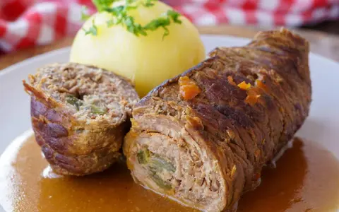 Herzhaftes Rouladen Rezept: Zarte Rinderrouladen mit Kartoffelklößen in einer kräftigen Soße, garniert mit Petersilie.