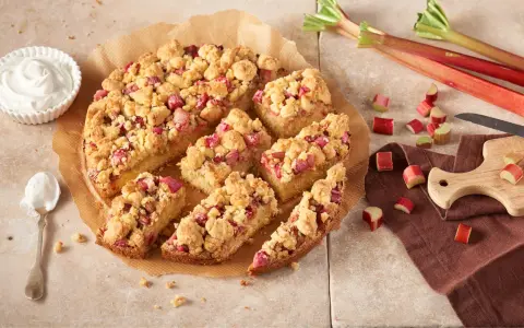 Ein saftiger Rhabarberkuchen mit Streuseln, perfekt für ein Rhabarberkuchen Rezept. Dazu eine Schüssel Schlagsahne.