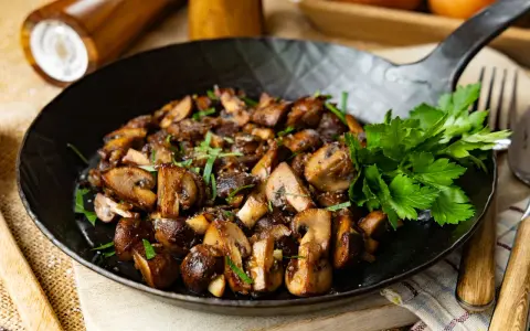 Gebratene Champignons in einer Pfanne, garniert mit frischer Petersilie. Ein köstliches Gericht, das zum Genießen einlädt.