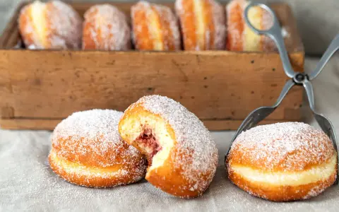 Zuckerüberzogene Berliner, eines davon mit Marmeladenfüllung, warten auf das nächste berliner rezept.
