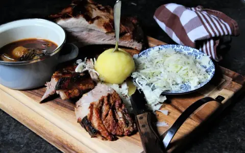 Deftige dicke Rippe mit Klößen, Sauerkraut und dunkler Soße auf Holzbrett.