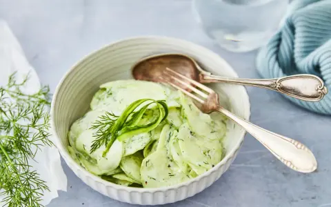 Omas Gurkensalat mit Joghurt, cremig und frisch, garniert mit Dill. Ein Löffel und eine Gabel liegen bereit.