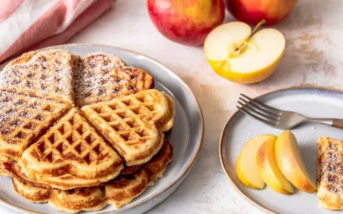 Herzförmige Waffeln mit Puderzucker, daneben frische Äpfel und Apfelspalten. Ein Genuss für alle Sinne!