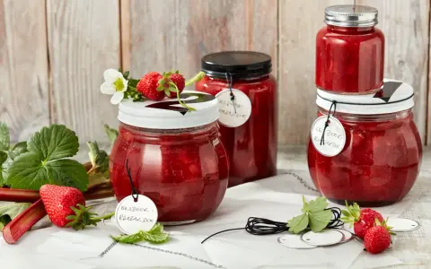 Gläser mit Erdbeer-Rhabarber-Marmelade, garniert mit frischen Erdbeeren und Blüten.