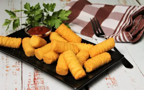 Goldbraune Kroketten, frisch zubereitet, liegen auf einem schwarzen Teller. Dazu gibt es Ketchup und frische Petersilie. Perfekt, um Kroketten selber machen zu lernen!