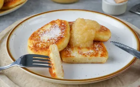 Goldbraune Quarkkeulchen, bestreut mit Puderzucker, serviert mit Apfelmus. Ein köstliches Quarkkeulchen Rezept zum Genießen.