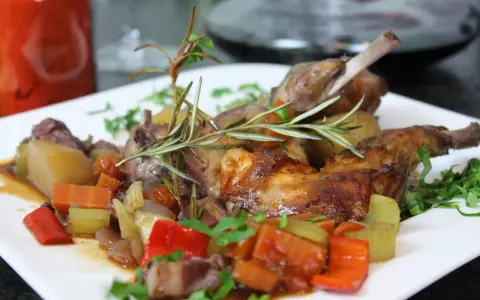 Klassisches Kaninchen-Rezept: Zartes Kaninchen mit Wurzelgemüse und Rosmarin auf einem weißen Teller serviert.