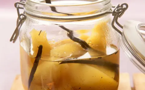 Ein Glas mit Quittenkompott, verfeinert mit Vanilleschoten. Die Fruchtstücke schimmern golden im Sirup.