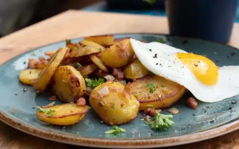 Bratkartoffeln mit Speck und einem Spiegelei, ein klassisches Rezept für ein herzhaftes Frühstück oder Abendessen.