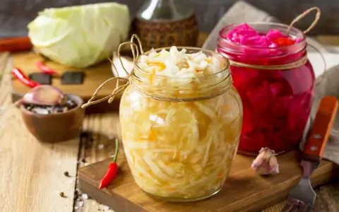 Zwei Gläser mit selbstgemachtem Sauerkraut und Rotkohl, daneben frischer Kohl, Knoblauch und Chilis.