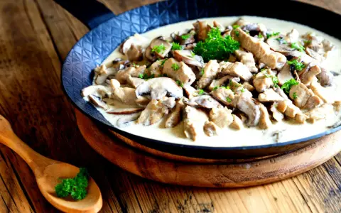 Putengeschnetzeltes mit Pilzen in cremiger Soße, garniert mit Petersilie, serviert in einer Pfanne auf rustikalem Holztisch.