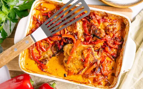 Herzhaftes Paprika Sahne Schnitzel in einer Auflaufform, mit roten Paprikastreifen und Zwiebeln in cremiger Sauce.