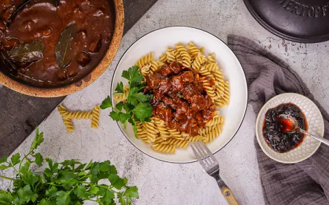 Herzhaftes Gulasch gemischt Rezept mit Fusilli, garniert mit Petersilie. Daneben ein kleiner Teller mit Preiselbeeren.