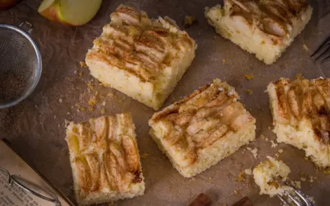 Saftige Apfel-Blechkuchen-Rezepte, bestreut mit Zimt. Ein Stück wird gerade mit einer Gabel probiert.