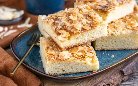 Original norddeutscher Butterkuchen mit Mandeln und Zucker bestreut, auf einem blauen Teller angerichtet.