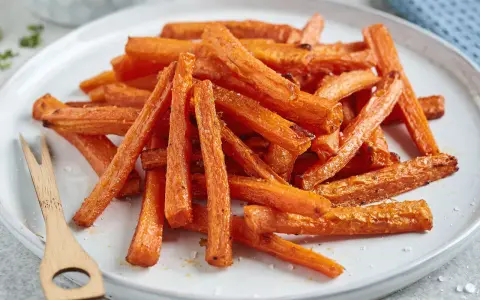 Knusprige karotten pommes, goldbraun gebacken, liegen auf einem Teller. Ein kleines Holzgabelchen liegt daneben.