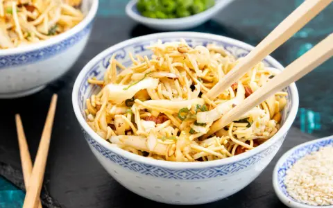 Ein Schüsselchen mit friss dich dumm Salat, Nudeln, Gemüse und Erdnüssen, bereit zum Genießen mit Stäbchen.