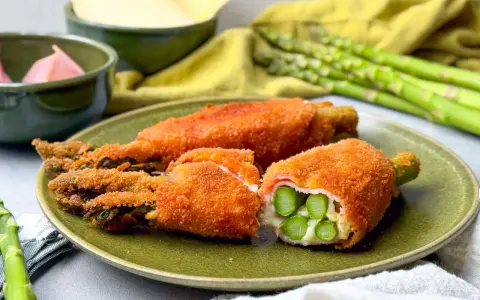 Knusprig paniertes Spargel Cordon Bleu mit Schinken und Käse gefüllt, auf einem grünen Teller angerichtet.