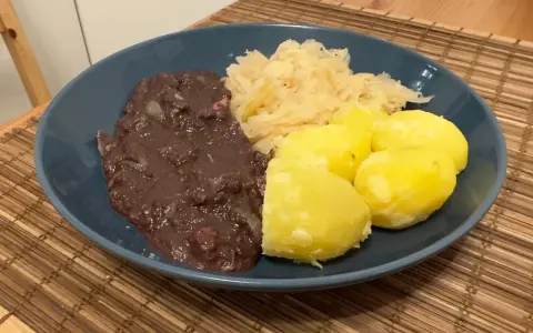 Ein Teller mit deftigem Essen: dunkle Soße, Sauerkraut und Salzkartoffeln. Erinnert an die gute, alte tote Oma.