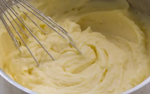 Cremiger kartoffelbrei ohne butter wird mit einem Schneebesen in einem Topf zubereitet.